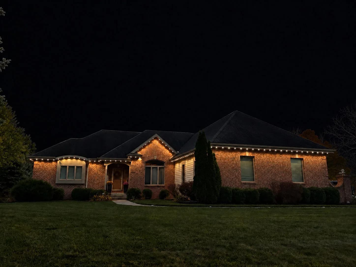 Real Kussmaul Co. permanent lighting in warm white along the gables and eaves of a brick ranch home at night