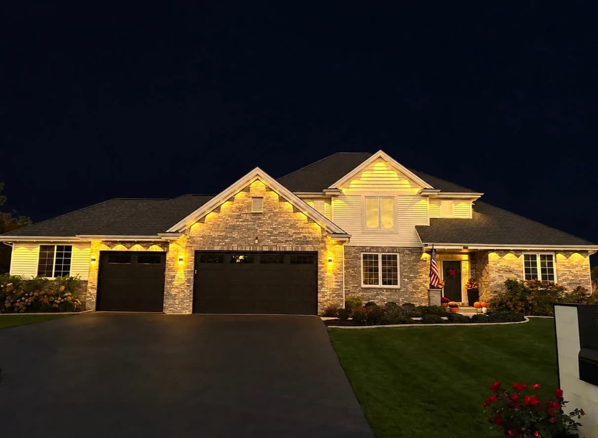 Real Kussmaul Co. permanent lighting in warm white along every gable and eave of a brick two-story home at night